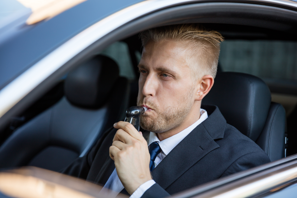 man using breathalyzer in car