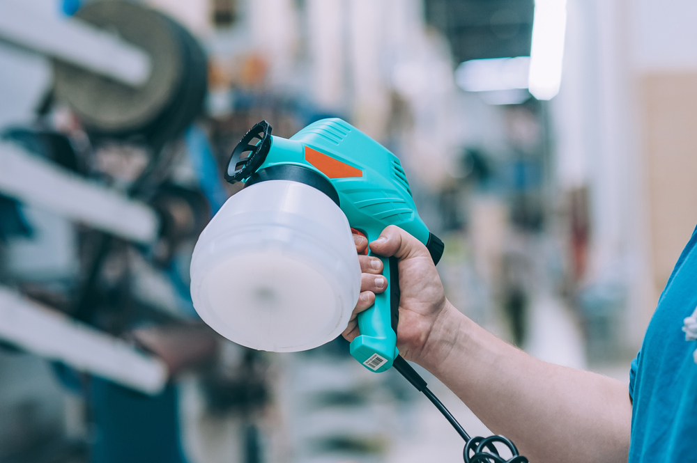 A man holds an electric spray gun in his hand