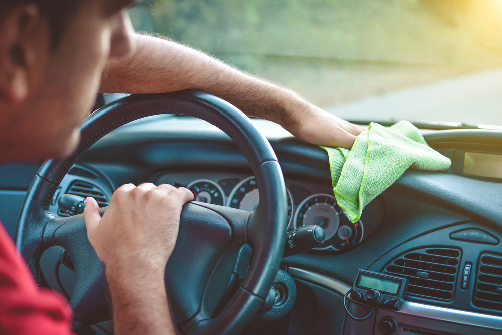 man trying to reach bottom of interior windshield with microfiber towel