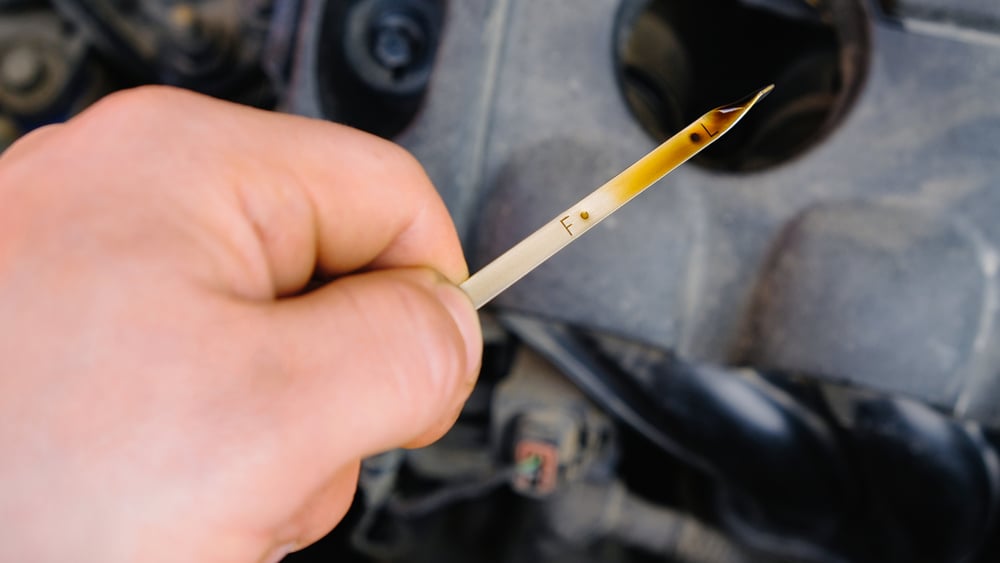 man checks car engine’s oil level with dipstick
