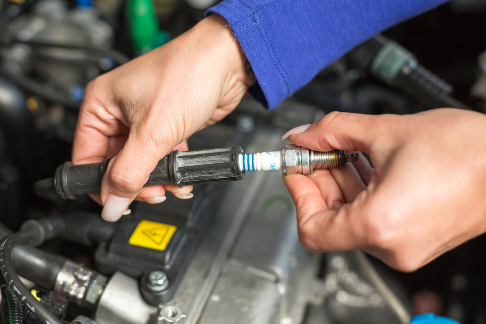 a mechanic changes a vehicle’s spark plug