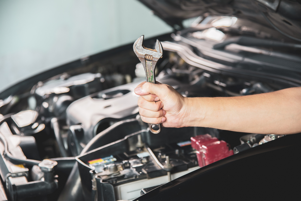 mechanic holding a wrench in front of a car