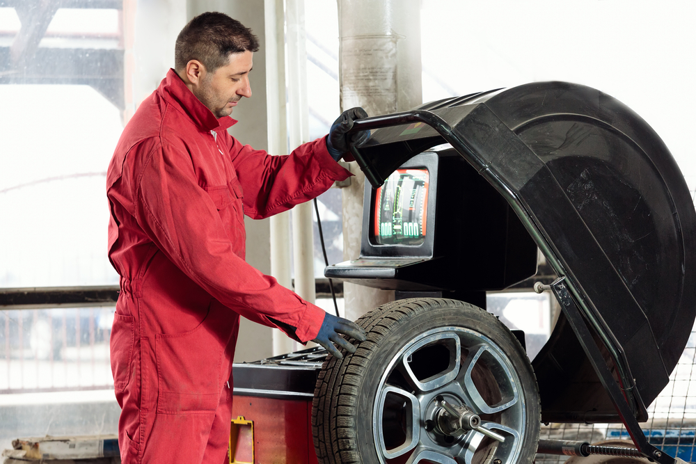 technician with gloves using a wheel balancing machine in a shop